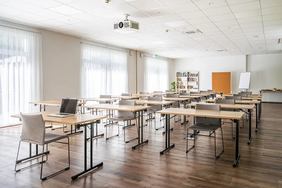 Tagungsraum mit Tischen und grauen Stühlen in Raumaufteilung